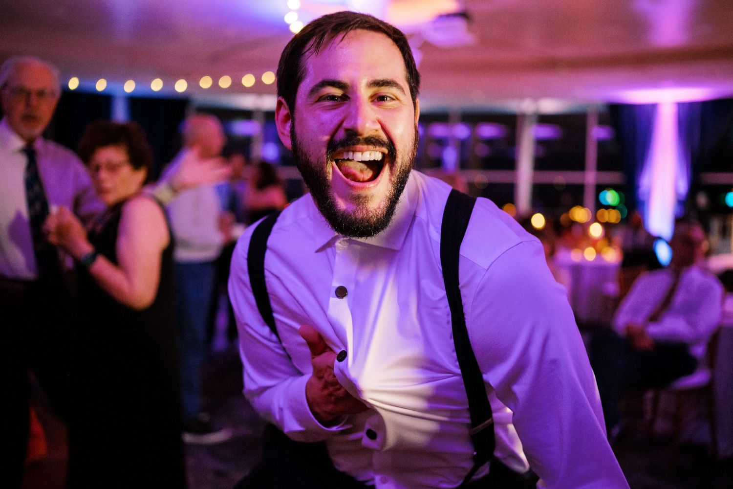 A guest enjoying himself on the dance floor at a wedding reception with purple lighting.