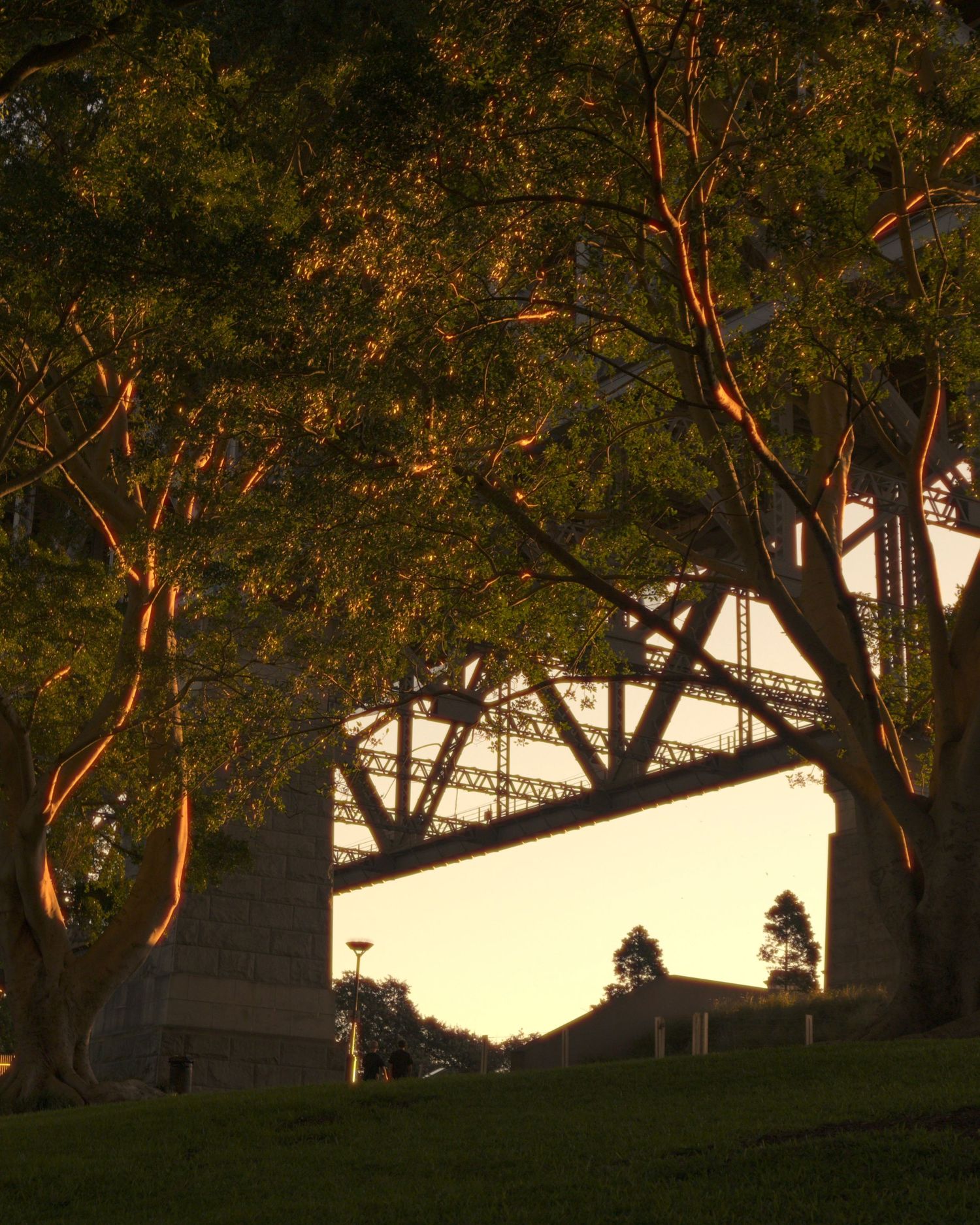Golden sunset light filters through trees revealing a large steel bridge structure in a city park.