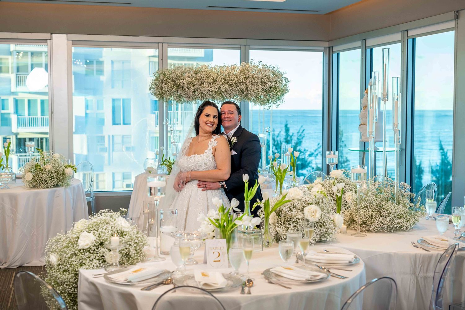 An elegant wedding reception room with ocean views and white table settings.