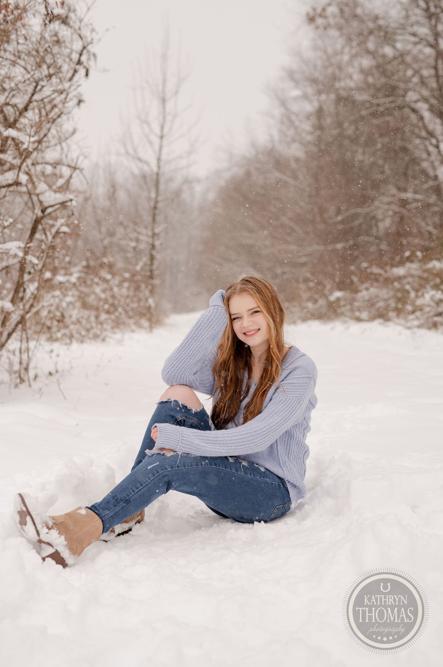 A person lounges in the snow wearing a cozy sweater and distressed jeans along a winter path.