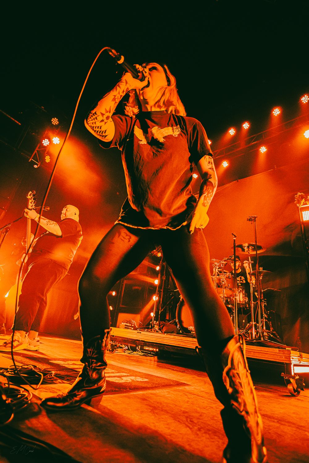 A performer sings passionately on stage bathed in dramatic orange lighting during an energetic concert performance.