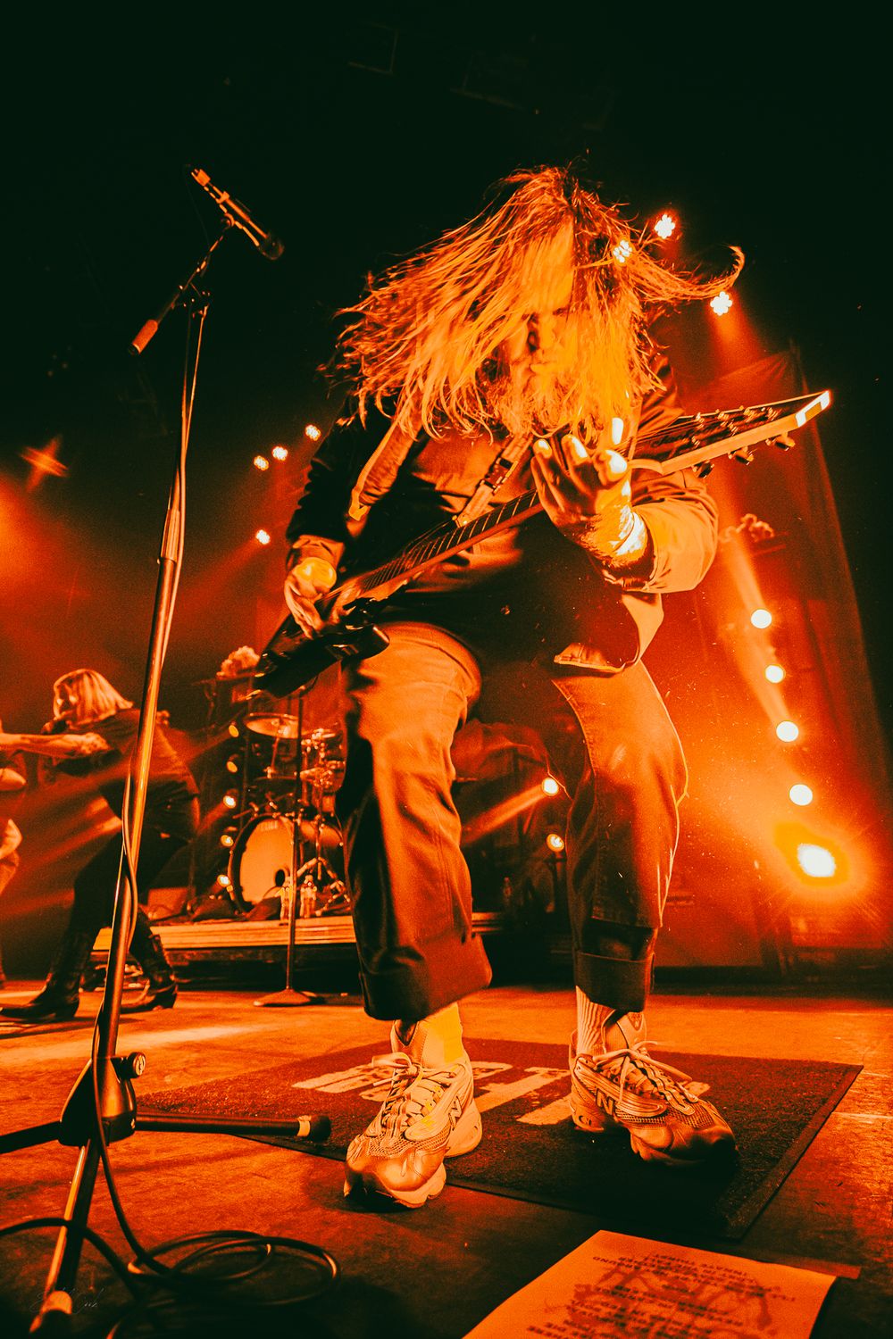 Energetic rock band performs on stage bathed in dramatic orange lighting during an intense live concert performance.