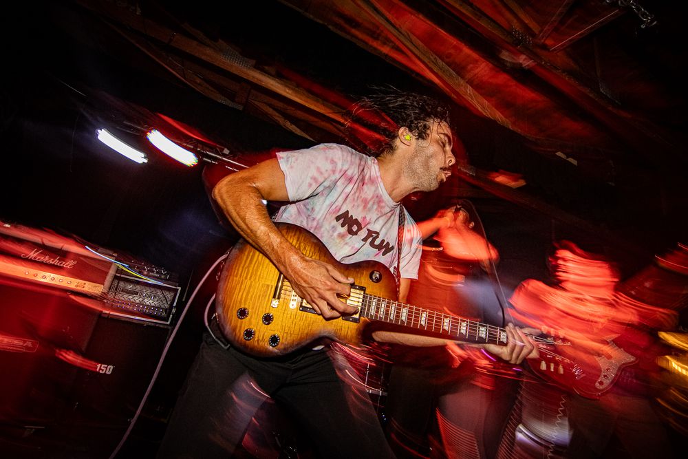 A guitarist performs on stage in dramatic red lighting during a live music performance.