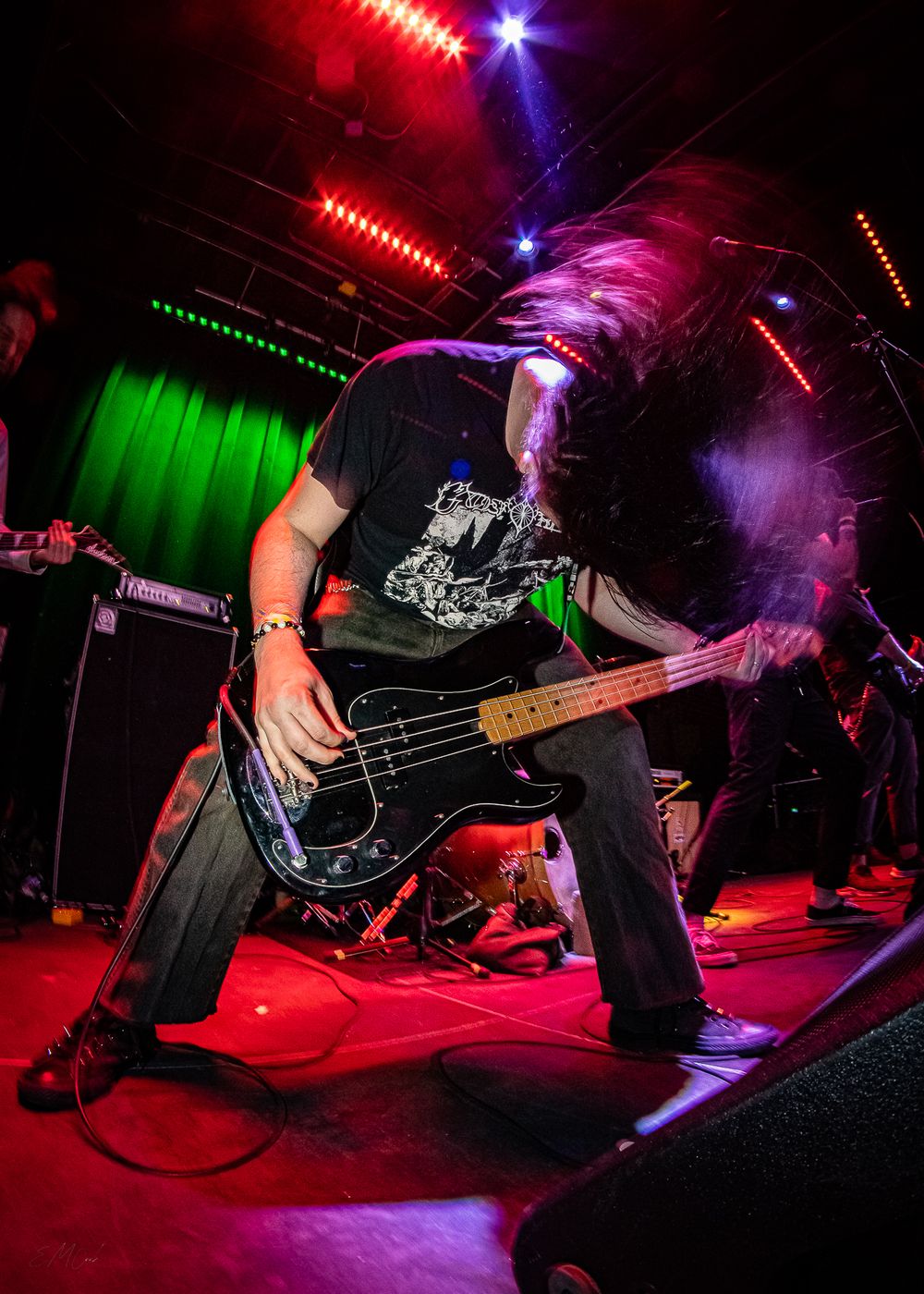Bass guitarist performing on stage with dynamic colored lighting and dramatic movement.