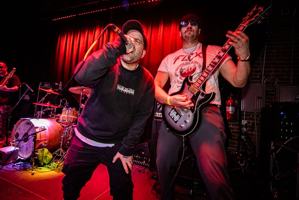 Energetic musicians perform at a dimly lit venue with red stage lighting creating a dynamic concert atmosphere.