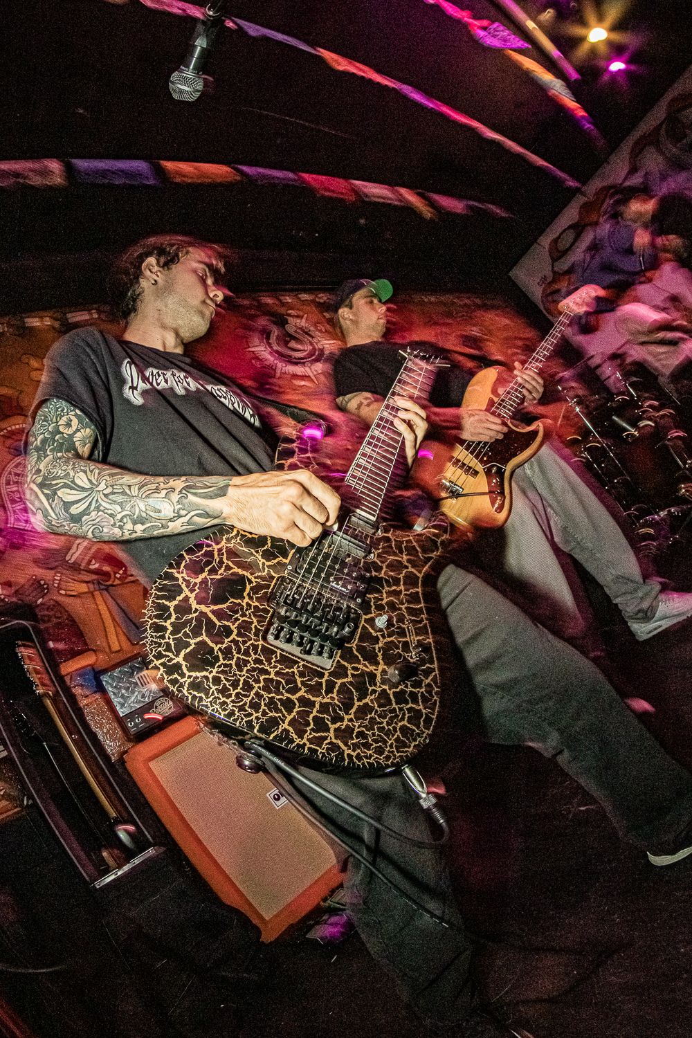 Guitarist performing on stage with decorated instrument under dramatic pink lighting.
