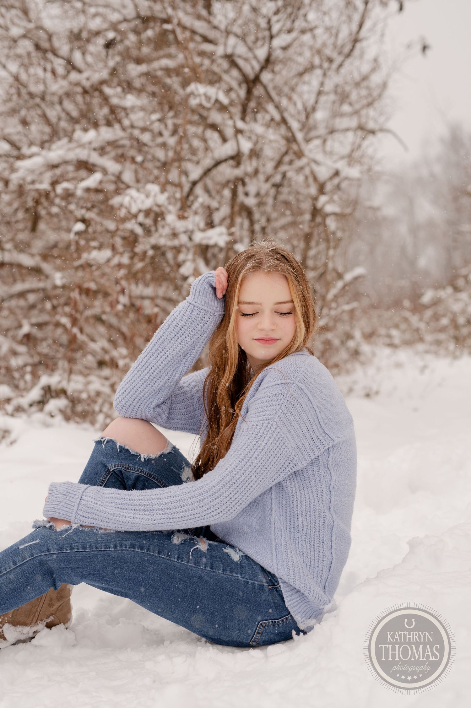 A person in a knit sweater and distressed jeans poses casually in a snowy winter setting.
