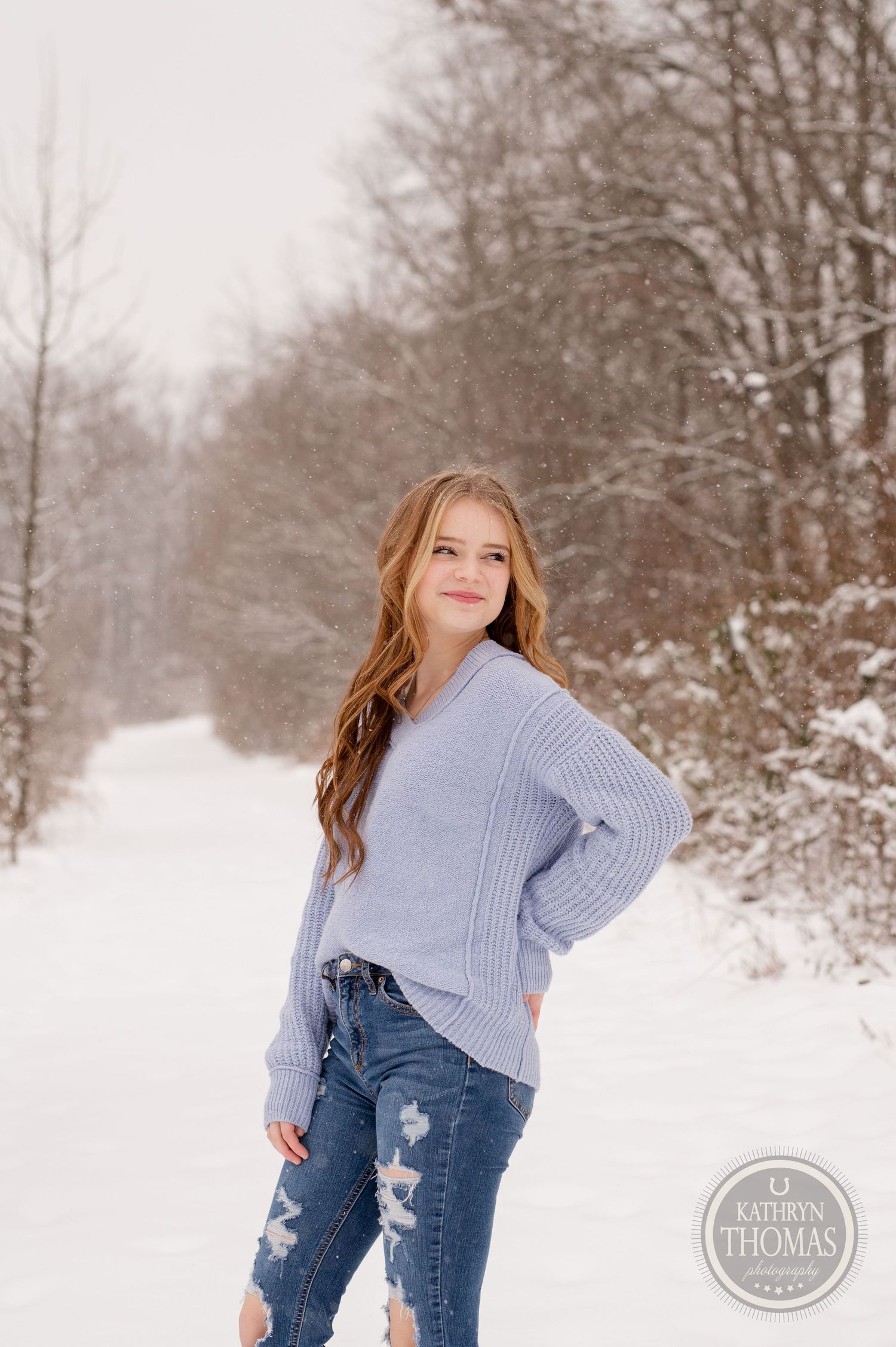 Portrait of person wearing blue knit sweater and ripped jeans in snowy setting.