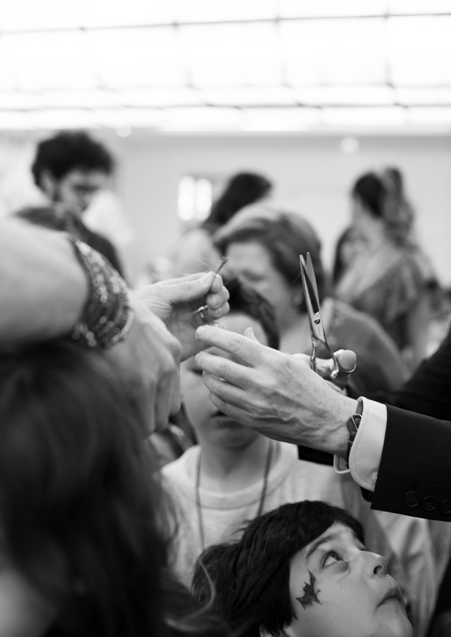 A black and white photograph showing people getting their hair styled and cut in a during the upsherin haircut chalake ceremony.
