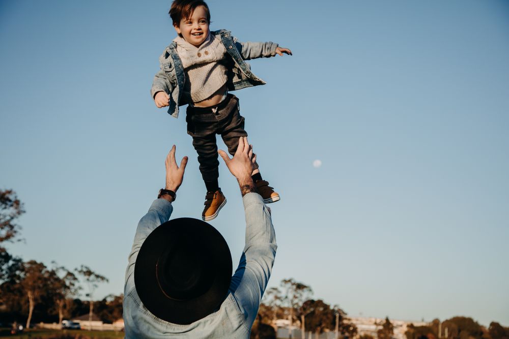 Joyful moment of someone tossing a child high in the air against a blue sky.