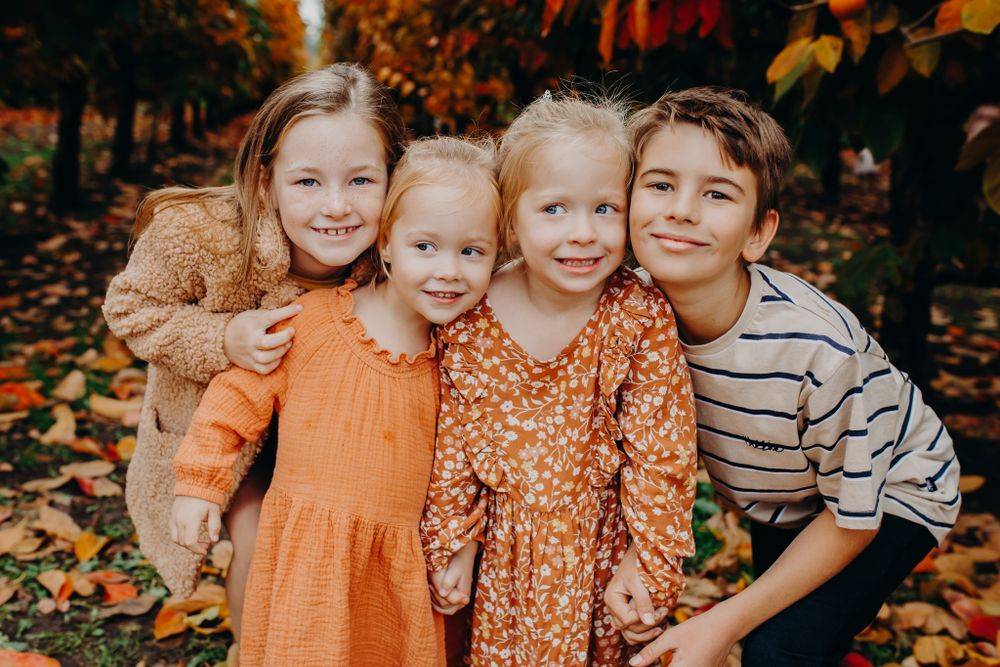 A group in coordinated fall outfits poses among autumn leaves.