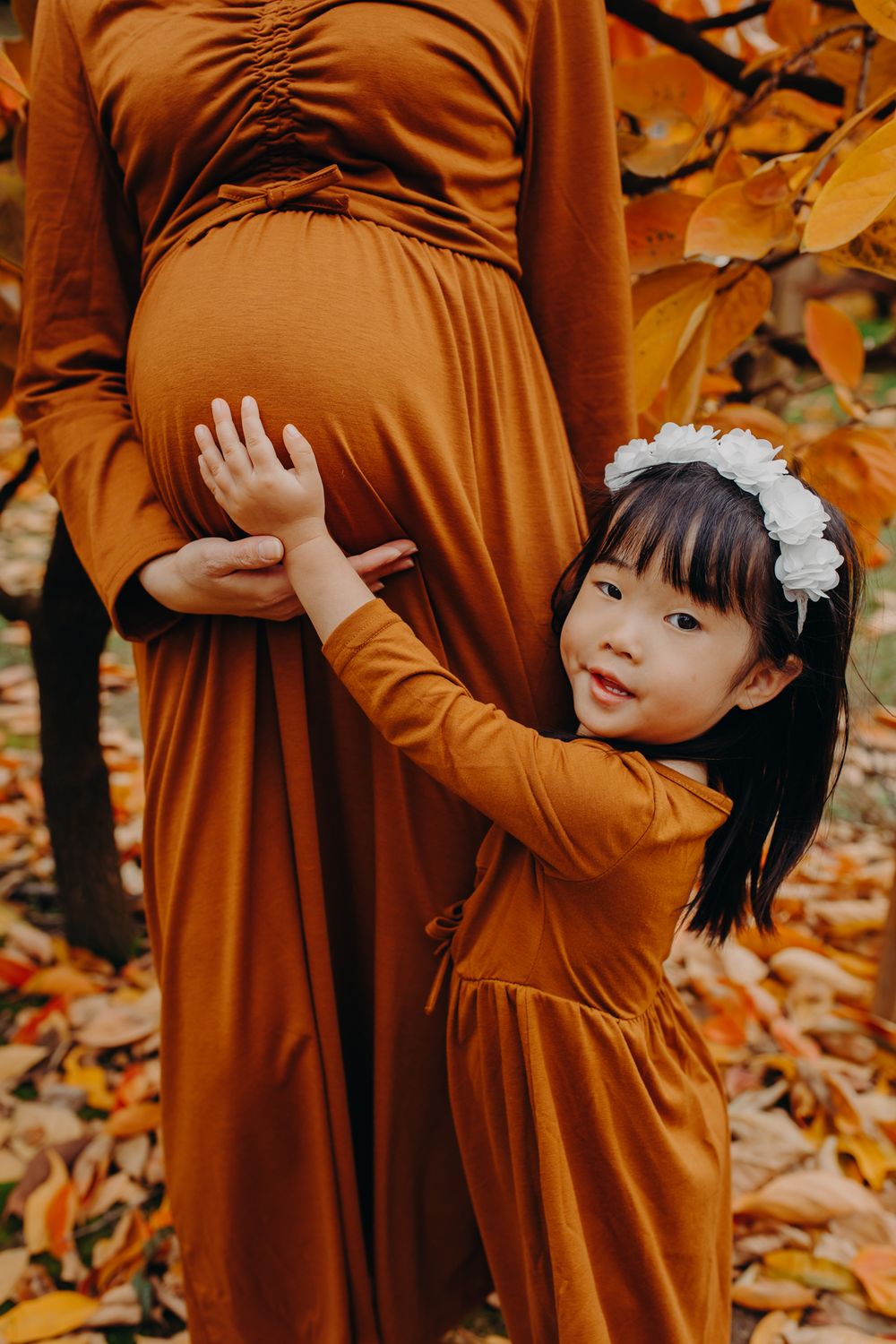 A touching autumn maternity moment with matching rust-colored dresses.