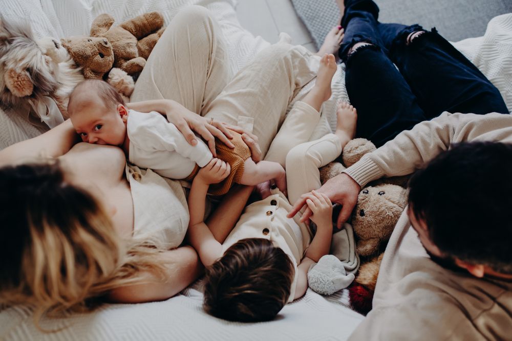 A cozy family cuddle session on white bedding with stuffed animals.