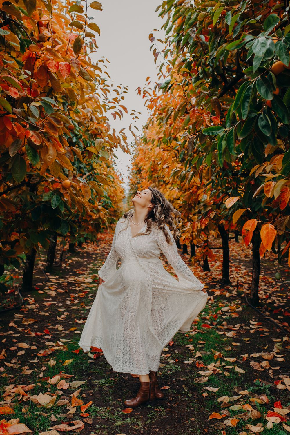 Woman in white dress twirling among autumn trees with orange leaves.