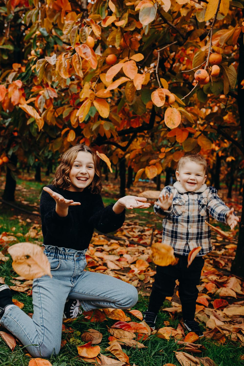 Playful children pose among fallen autumn leaves in casual outfits.