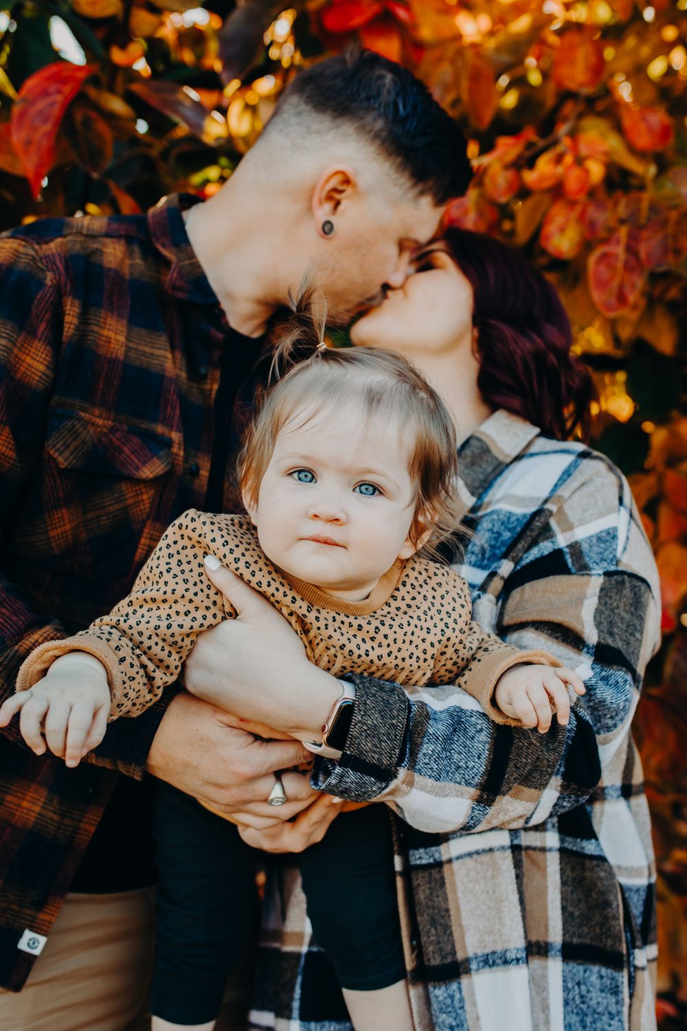 Family portrait with autumn leaves and plaid flannel clothing in warm golden light.