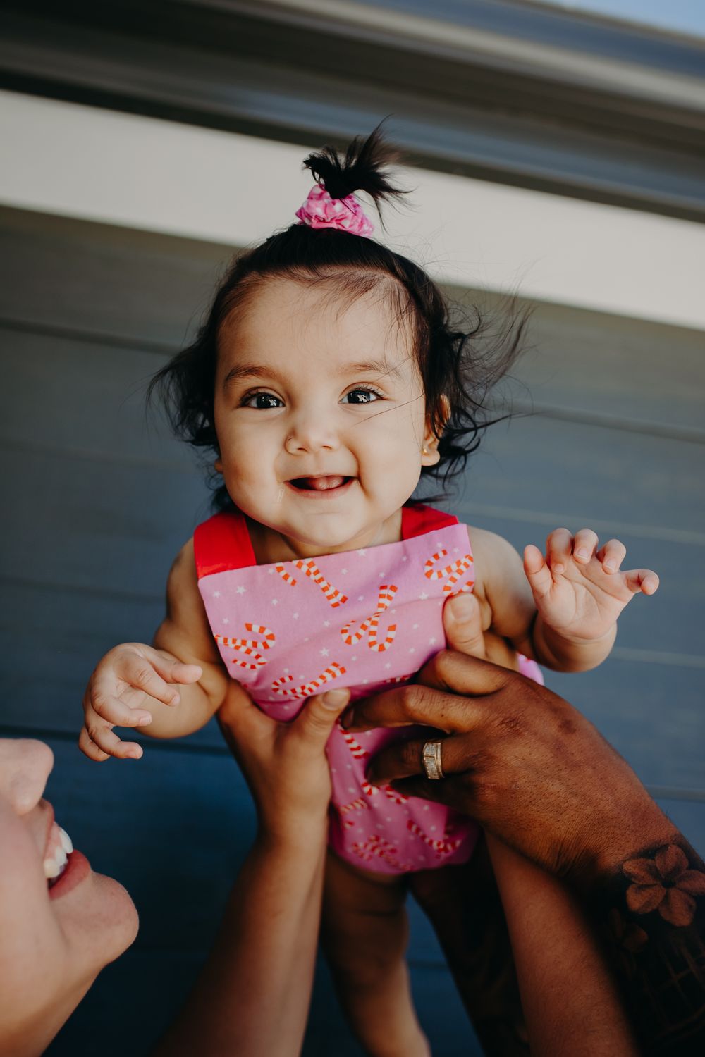 Happy baby wearing pink bib being held up against blue background.