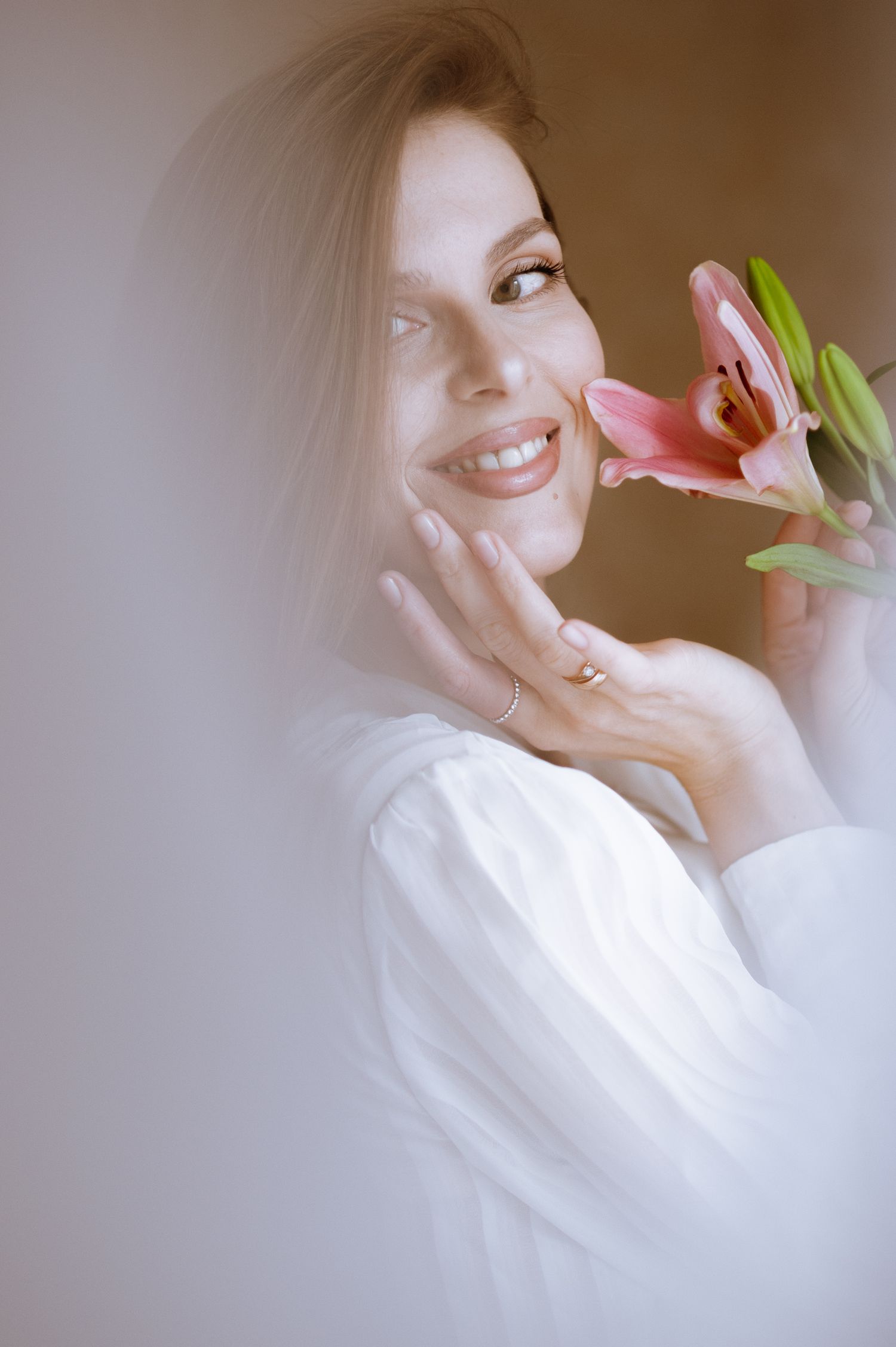 Soft feminine portrait in white holding pink flowers with dreamy natural lighting.