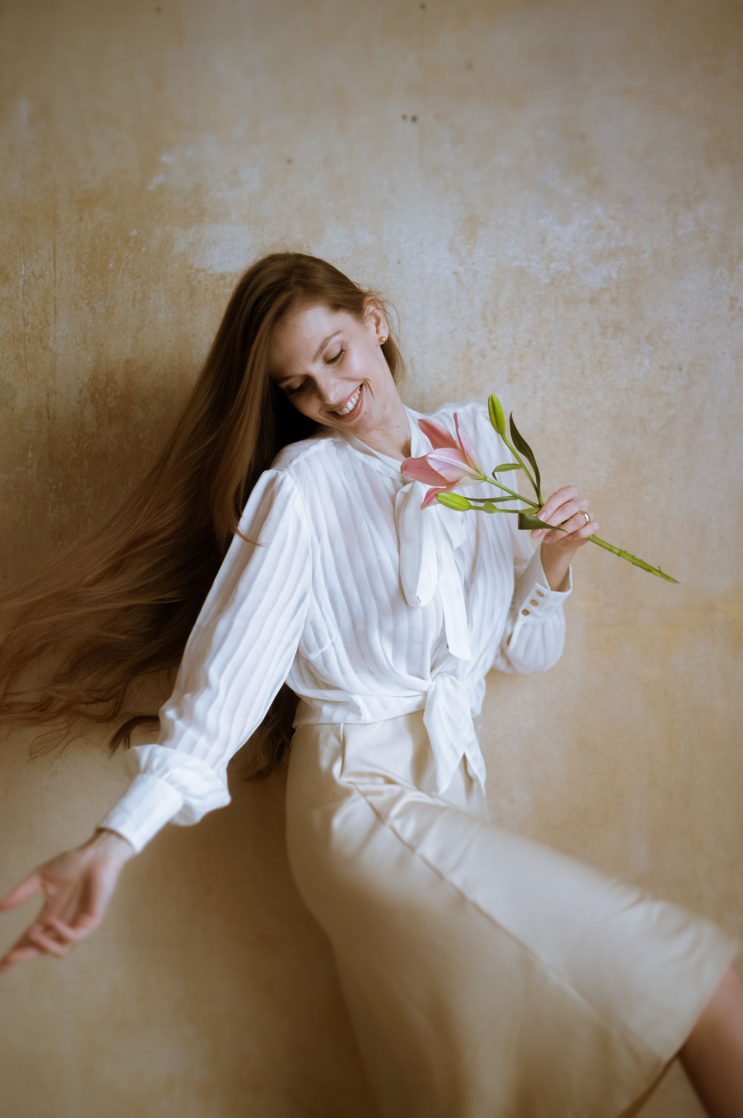 Artistic portrait series showing figure in white clothing with lily flower against neutral wall.