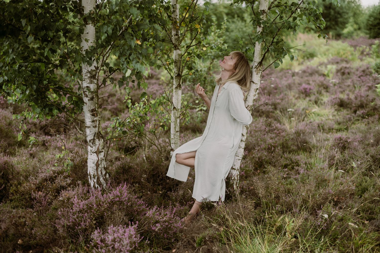 Person in flowing white dress walks through blooming spring garden with pink flowers and green foliage.