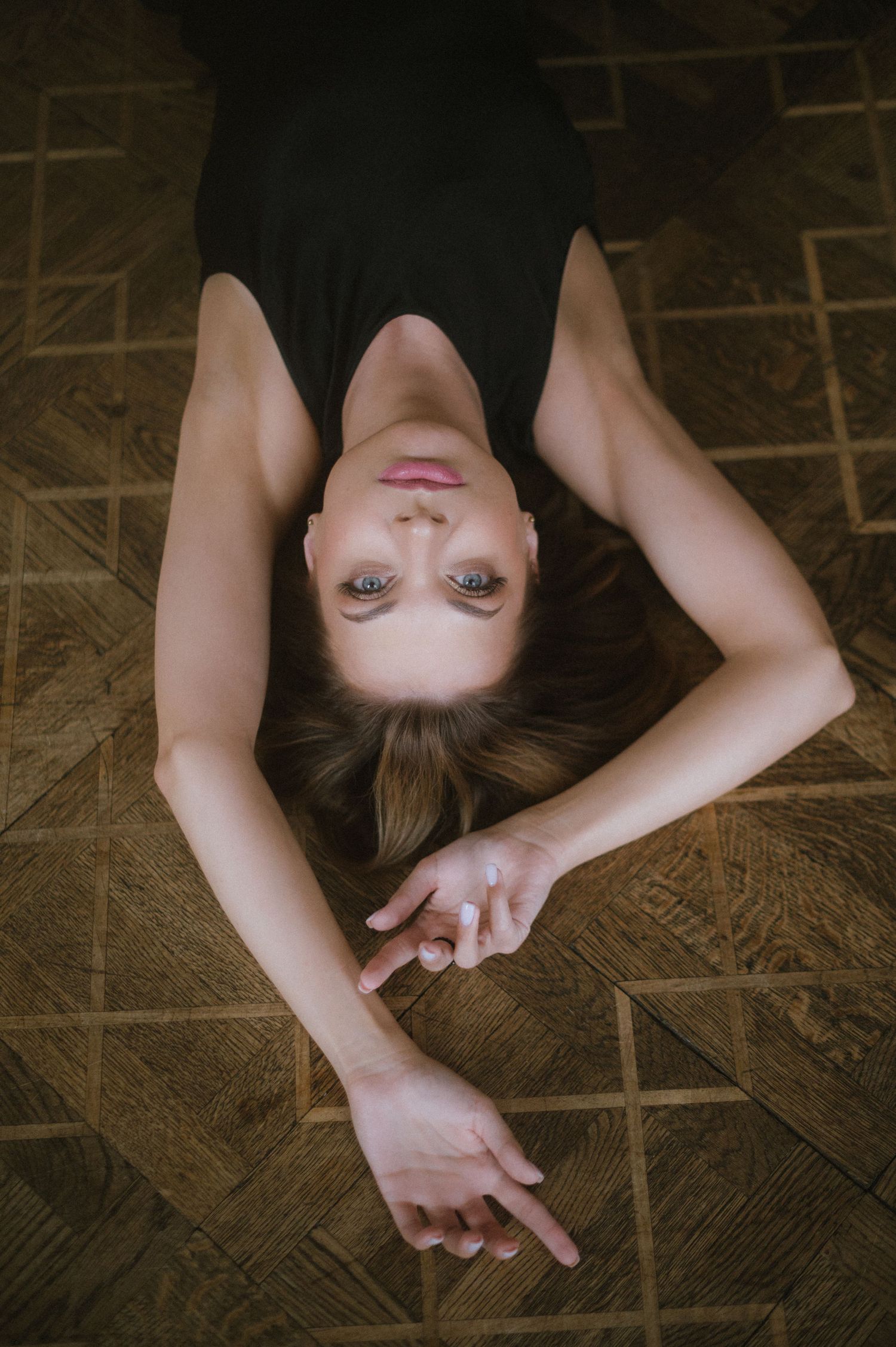 Overhead view of a figure lying on dark wooden flooring in artistic poses.