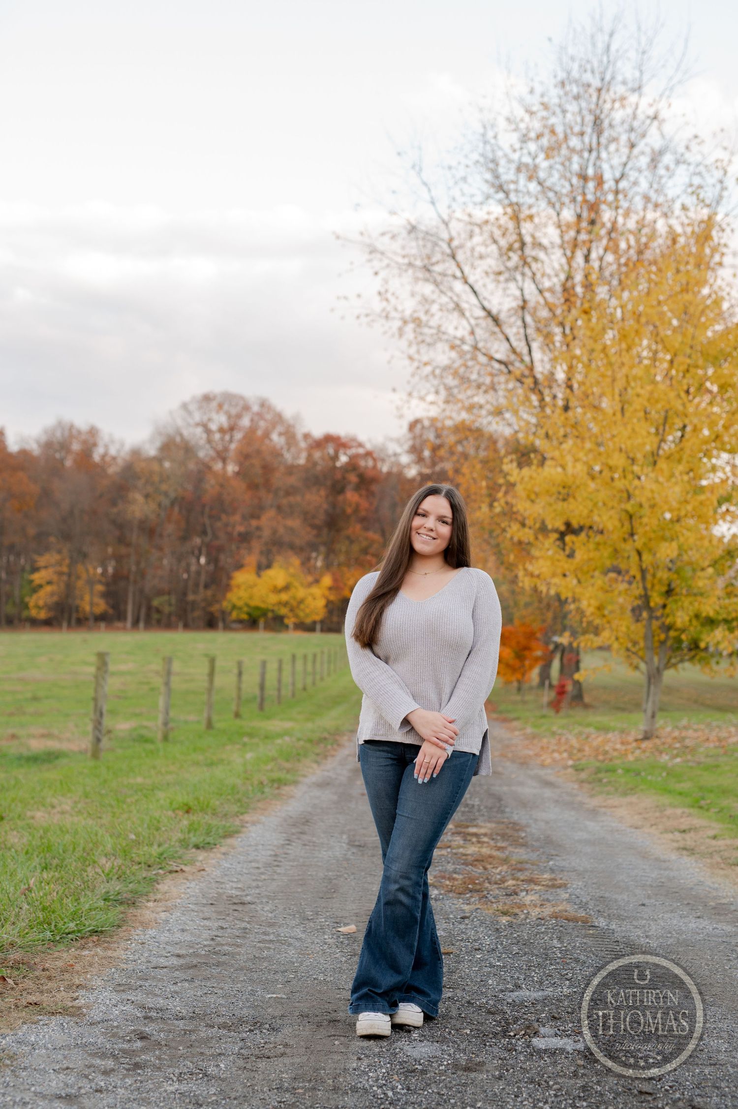 A casual autumn portrait on a dirt path with yellow trees and fenced pastures in the background.