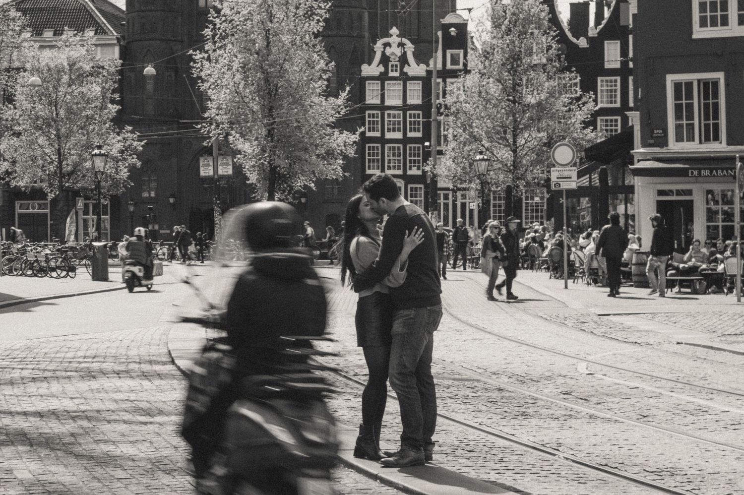 Black and white street scene showing people walking on cobblestone streets in Amsterdam.