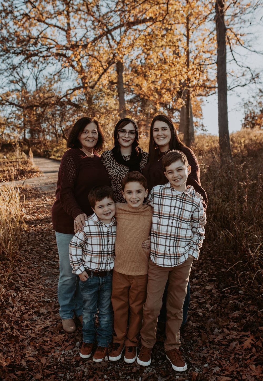 A casual family gathering captured outdoors among fallen autumn leaves and tall trees.