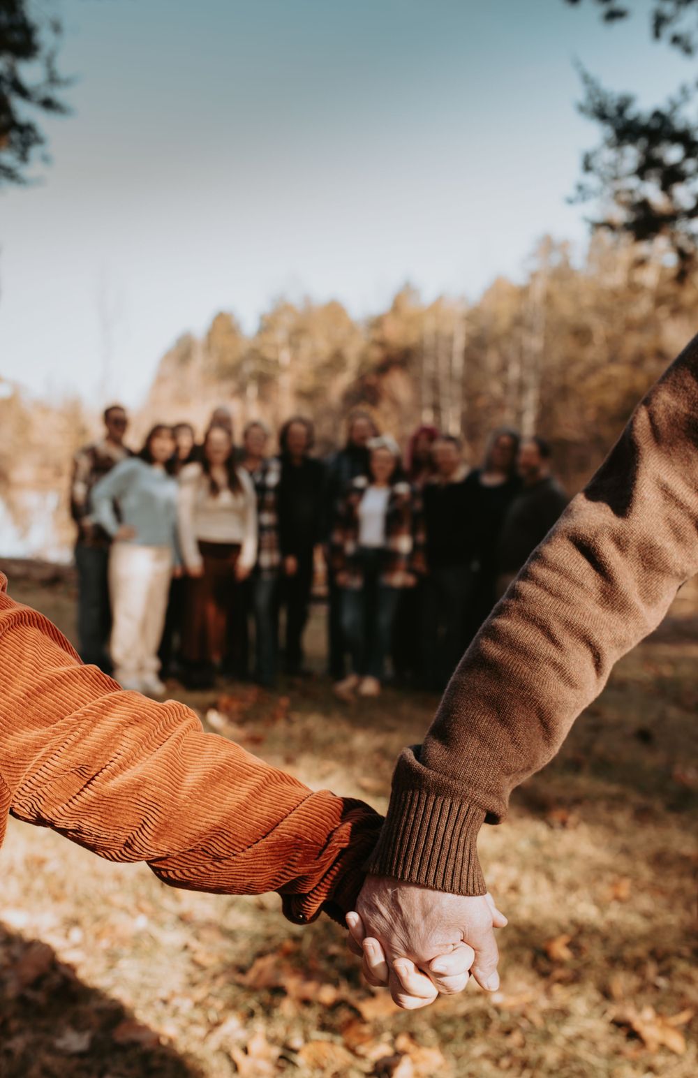 Hands holding in an autumn outdoor setting with group blurred in background.