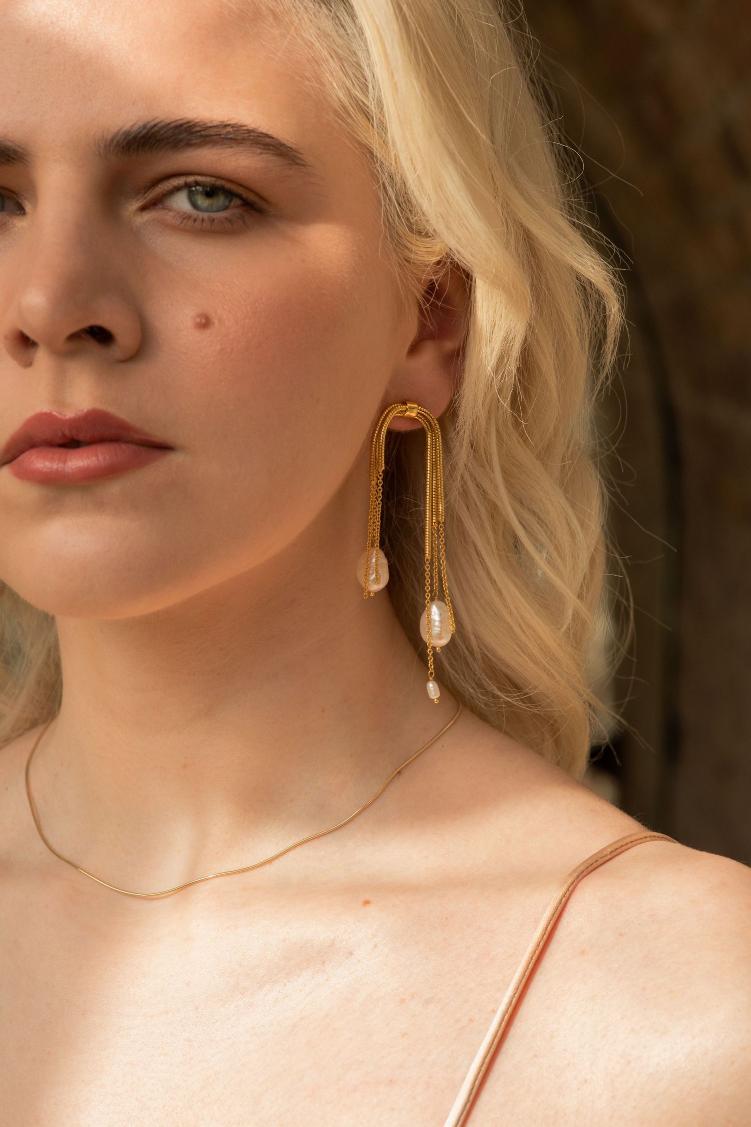Close-up shot showcasing geometric gold earrings with pearl details.