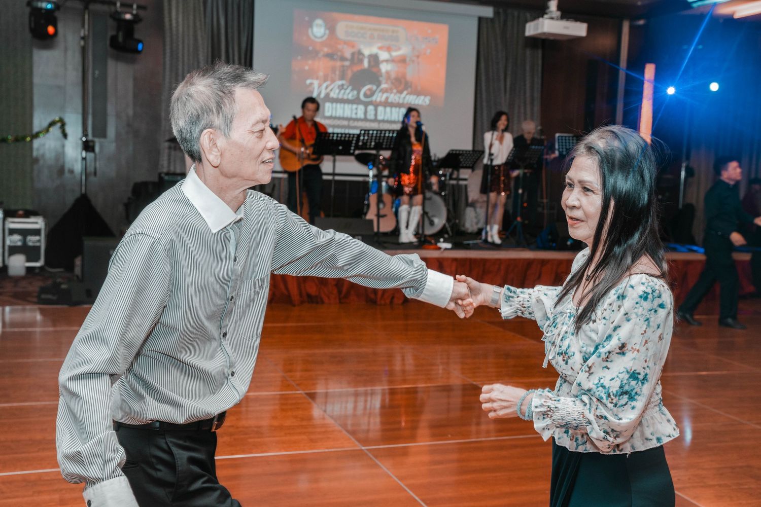 Two people dancing together on wooden floor during social dance event with band performing.