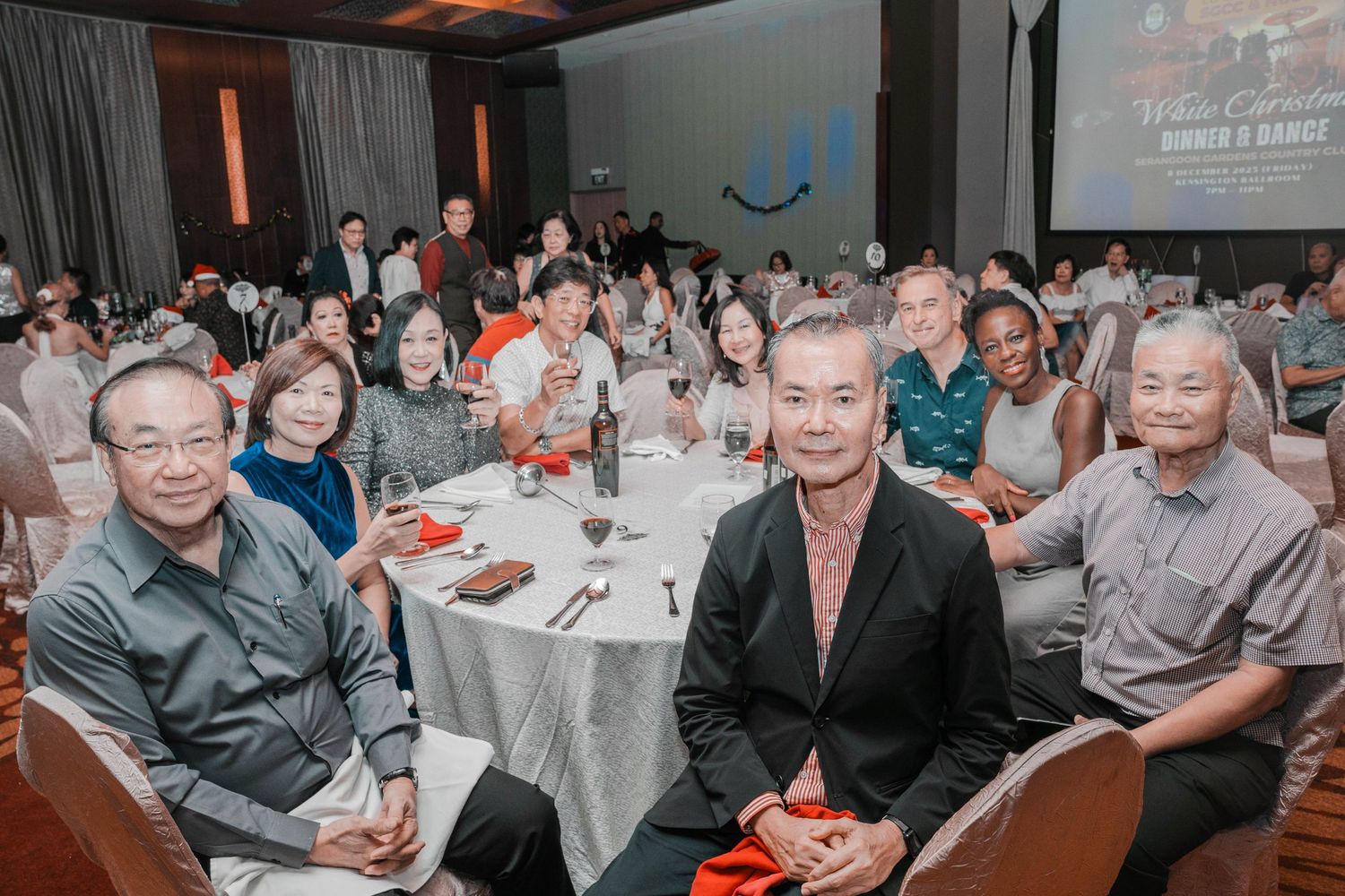 Guests seated at round tables during a formal dinner event with projection screen in background.