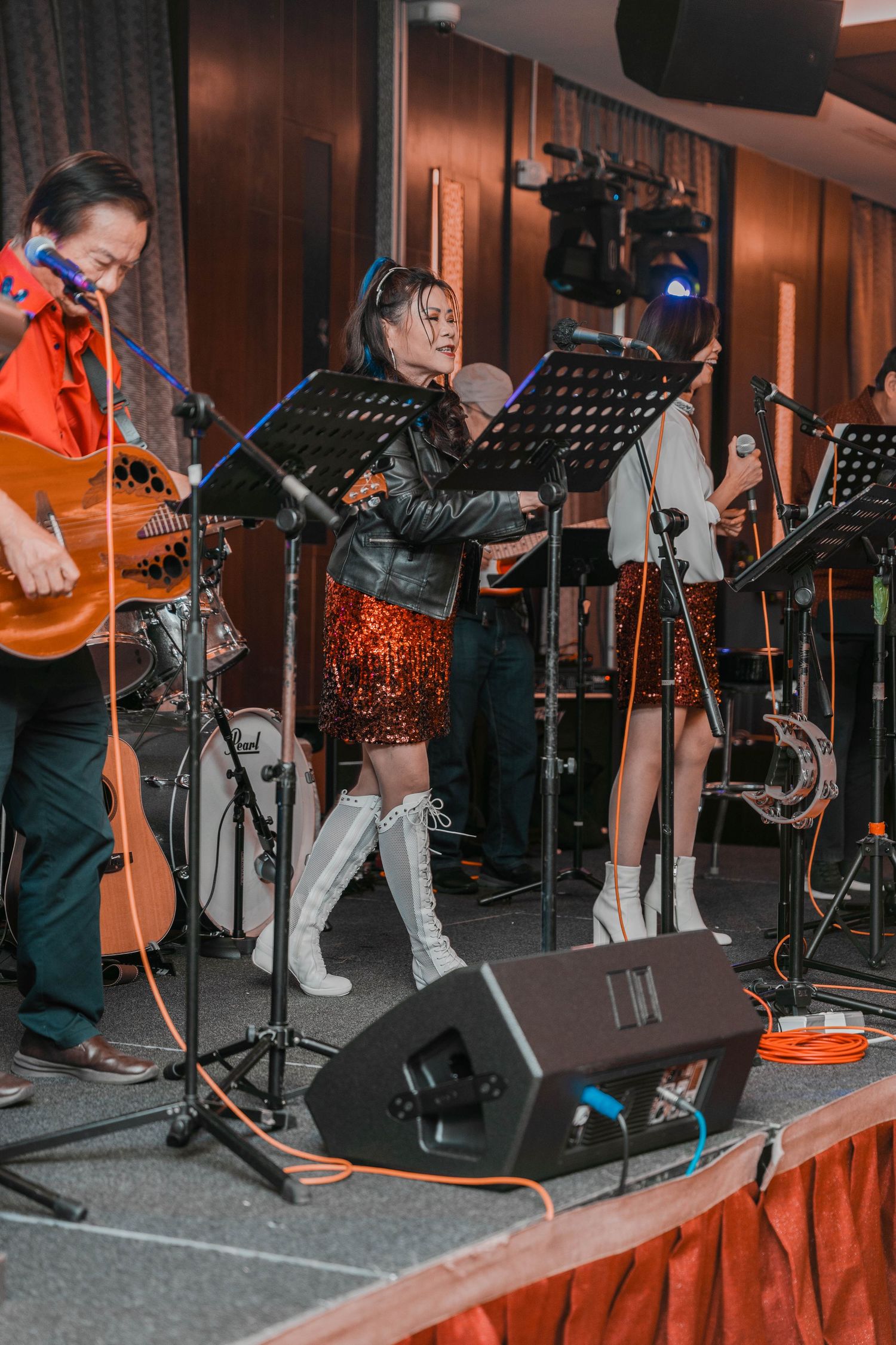 Musicians performing on stage with singer in boots and guitarist at formal event.