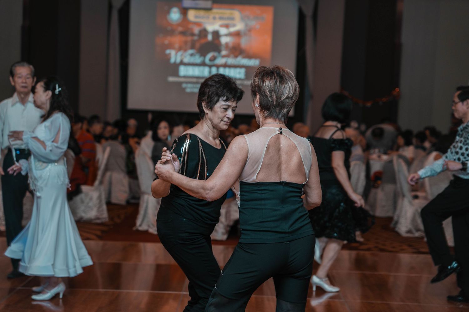 Couples dancing in formal attire on a wooden dance floor at an evening event.