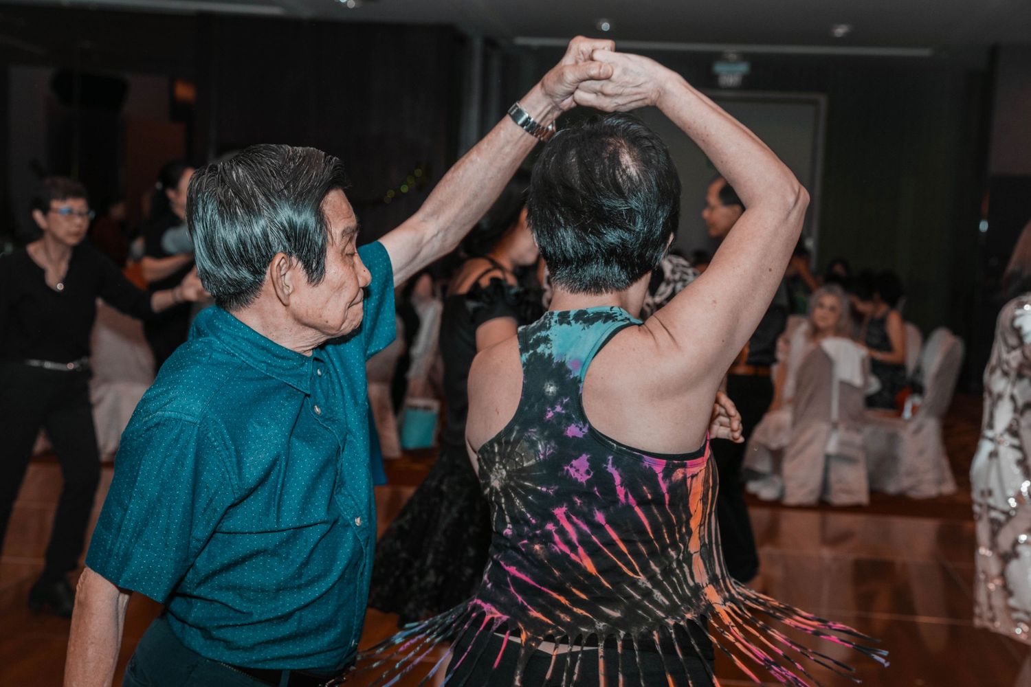 Two people dancing together in turquoise and patterned outfits on dance floor.
