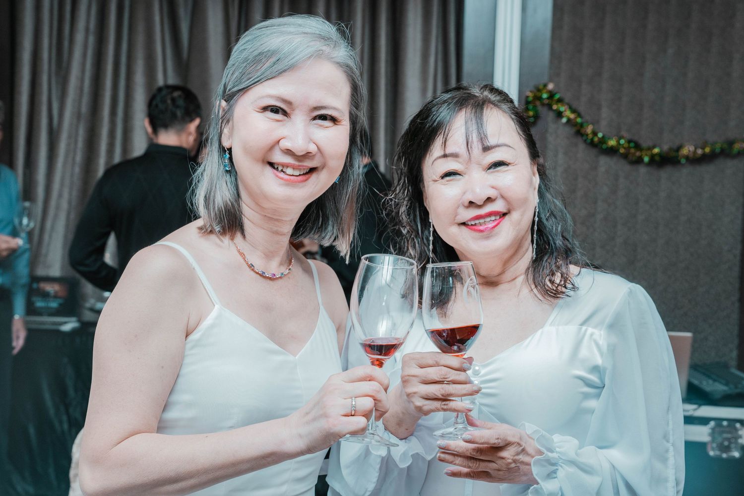 Two women in elegant attire toasting with wine glasses at an evening celebration.