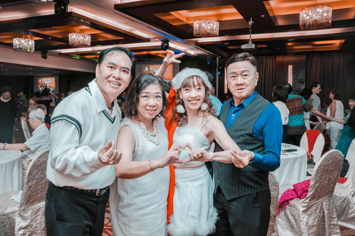 A group of guests posing together at a wedding reception in a banquet hall with elegant lighting.