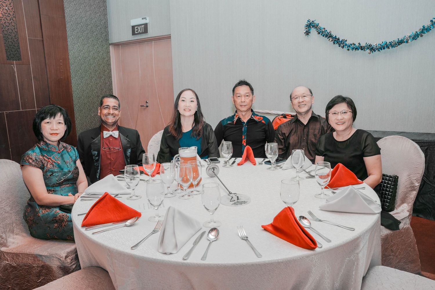 Group of guests seated at a round table with formal place settings and red napkin accents.