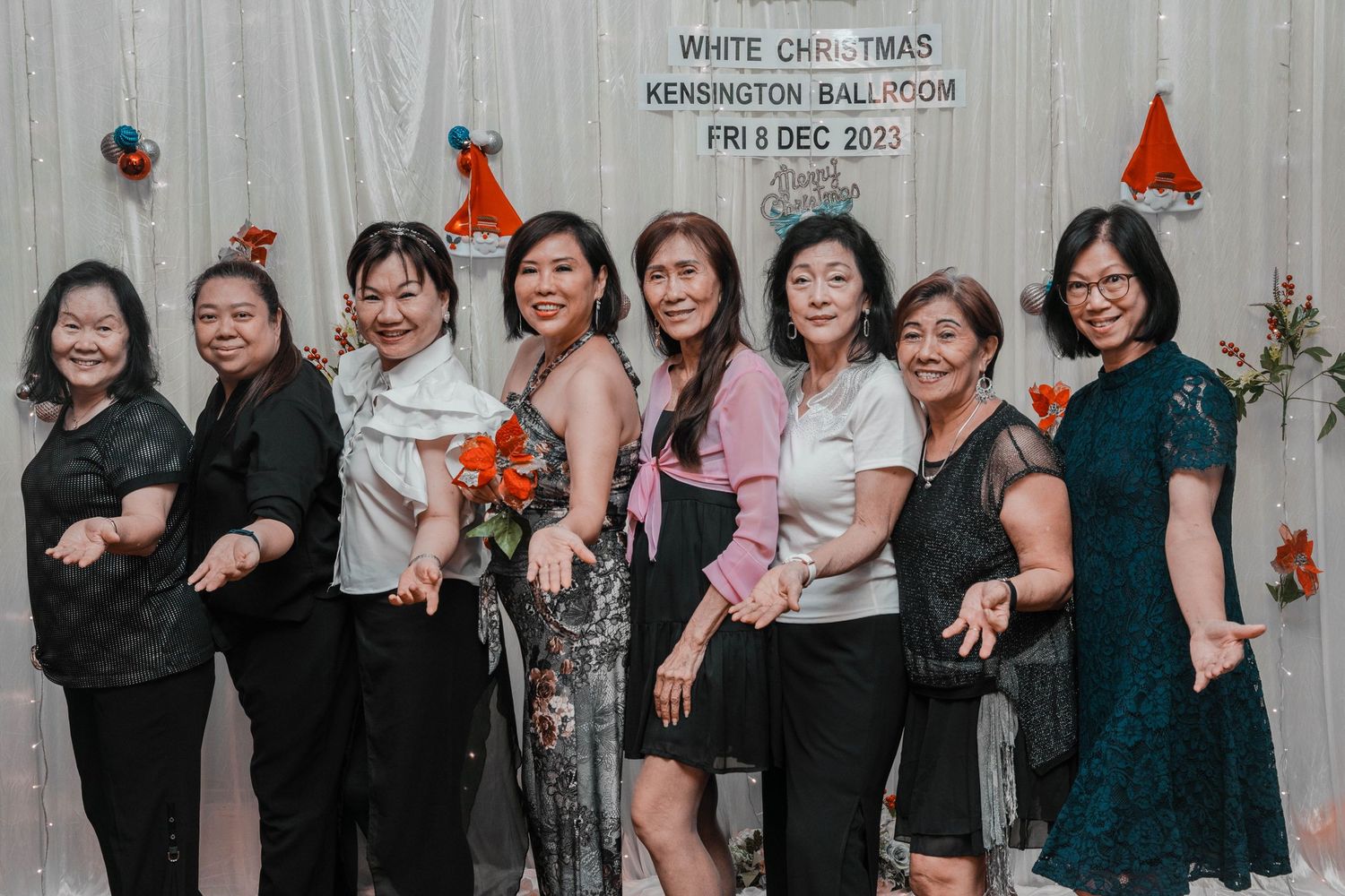 Women in formal attire posing against a decorated wall with Christmas ornaments.