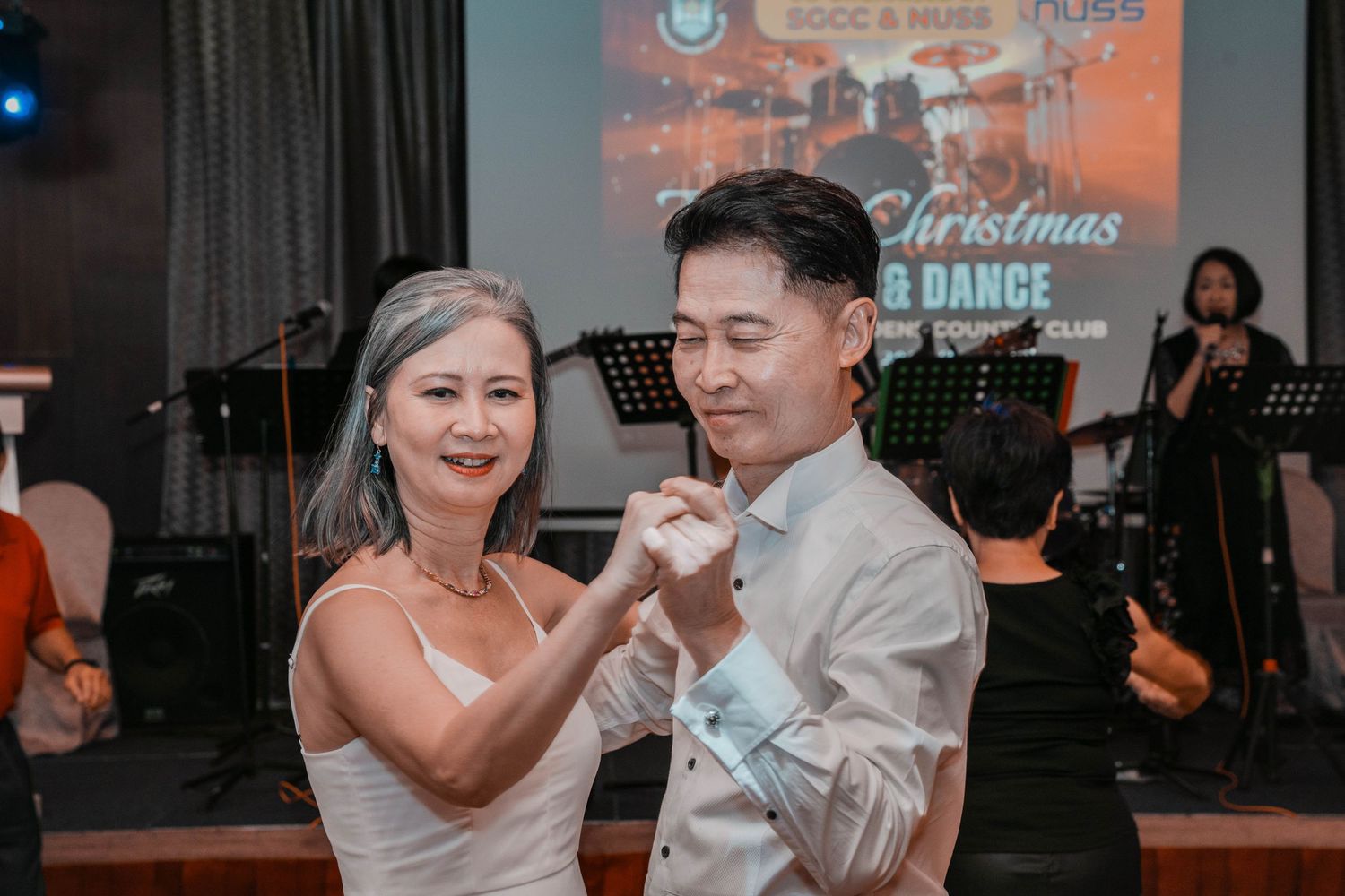 A couple dancing together at a Christmas-themed event with stage and band visible in background.