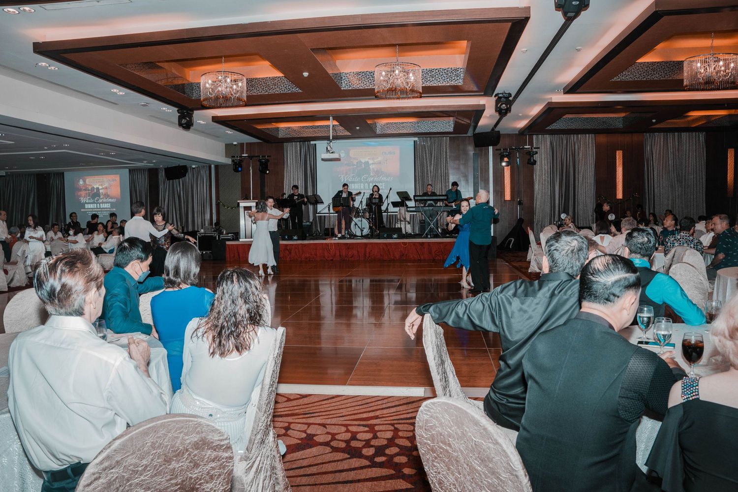 Wide shot of a formal event space with guests seated at round tables and wooden dance floor.