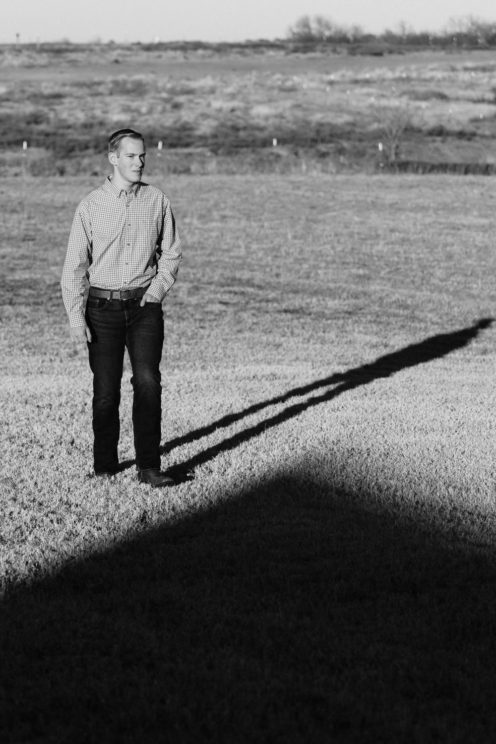 Person standing in field casting long shadow during golden hour.
