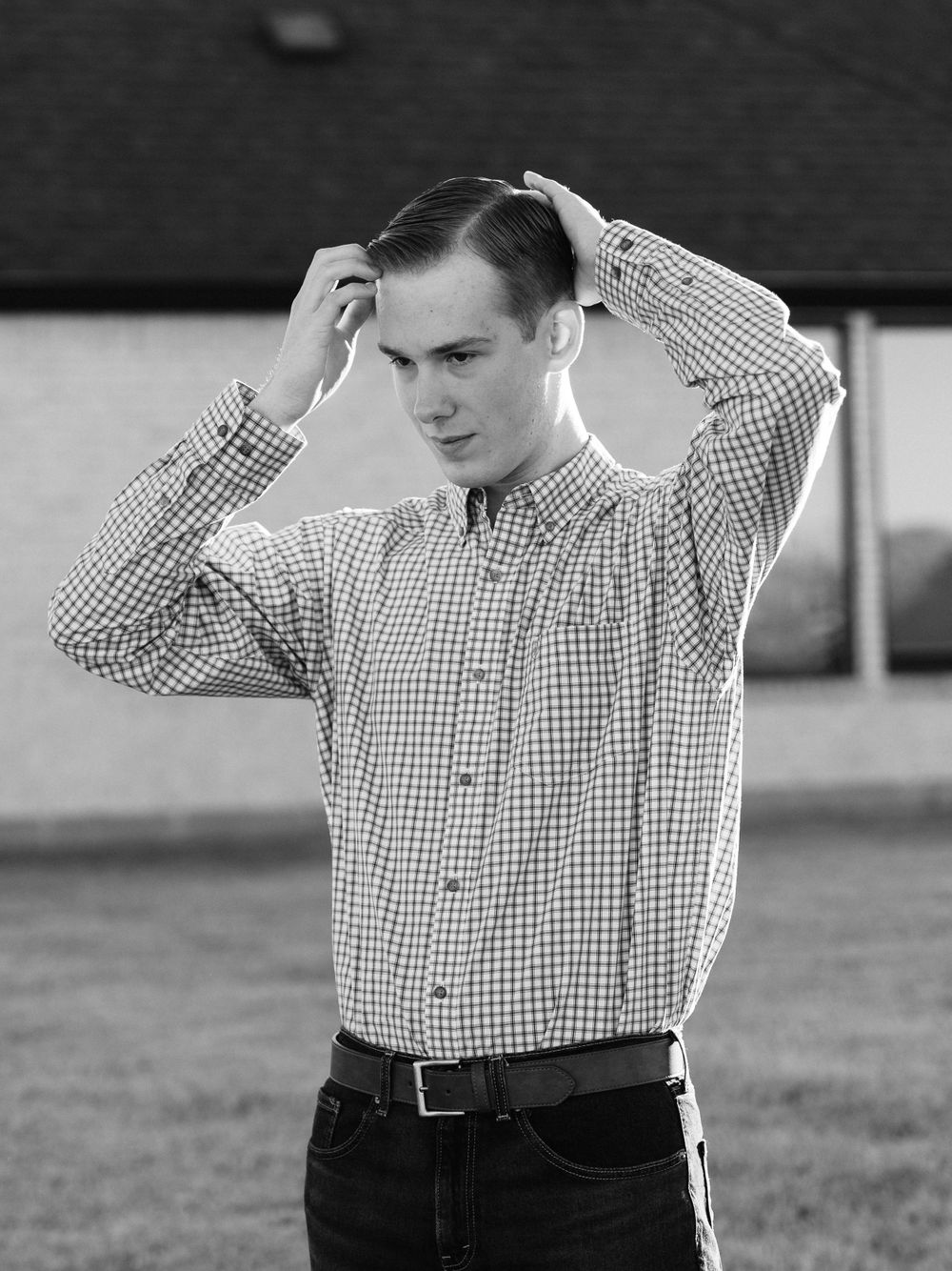 Person in checkered shirt adjusting hair outdoors in black and white photo.