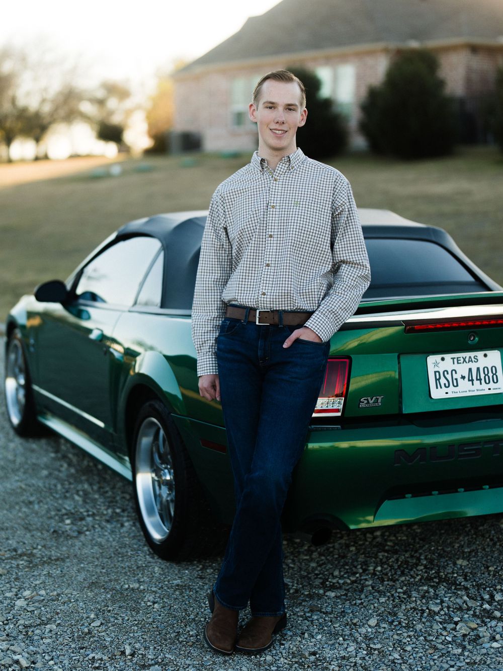 Green Ford Mustang SVT Cobra parked in front of suburban house at sunset.