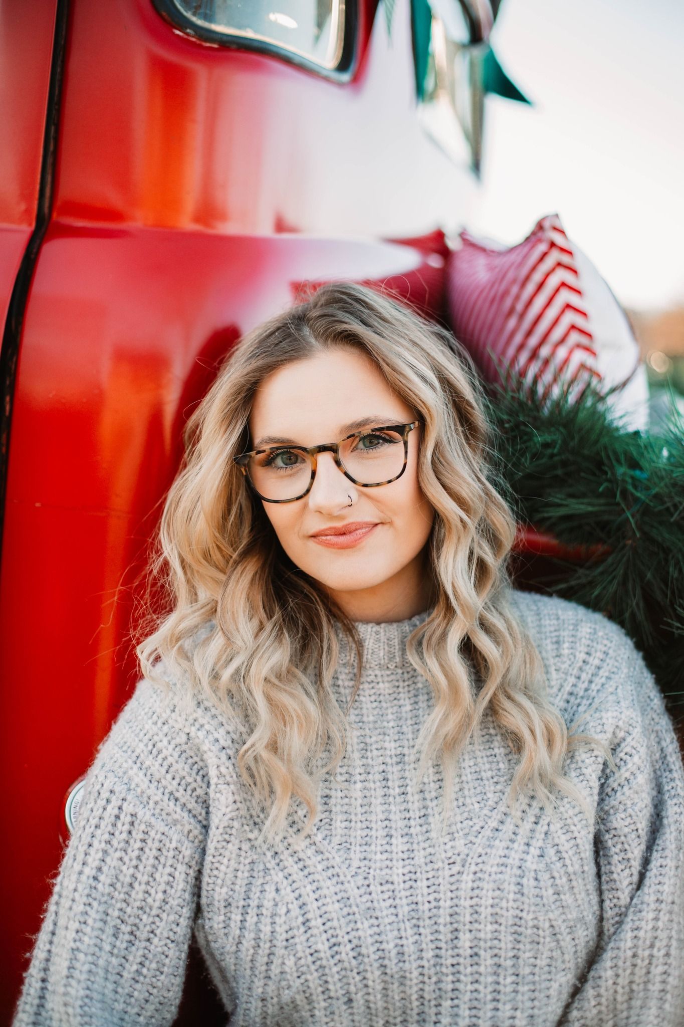 Portrait series of someone wearing glasses and a cozy gray sweater against a red background.