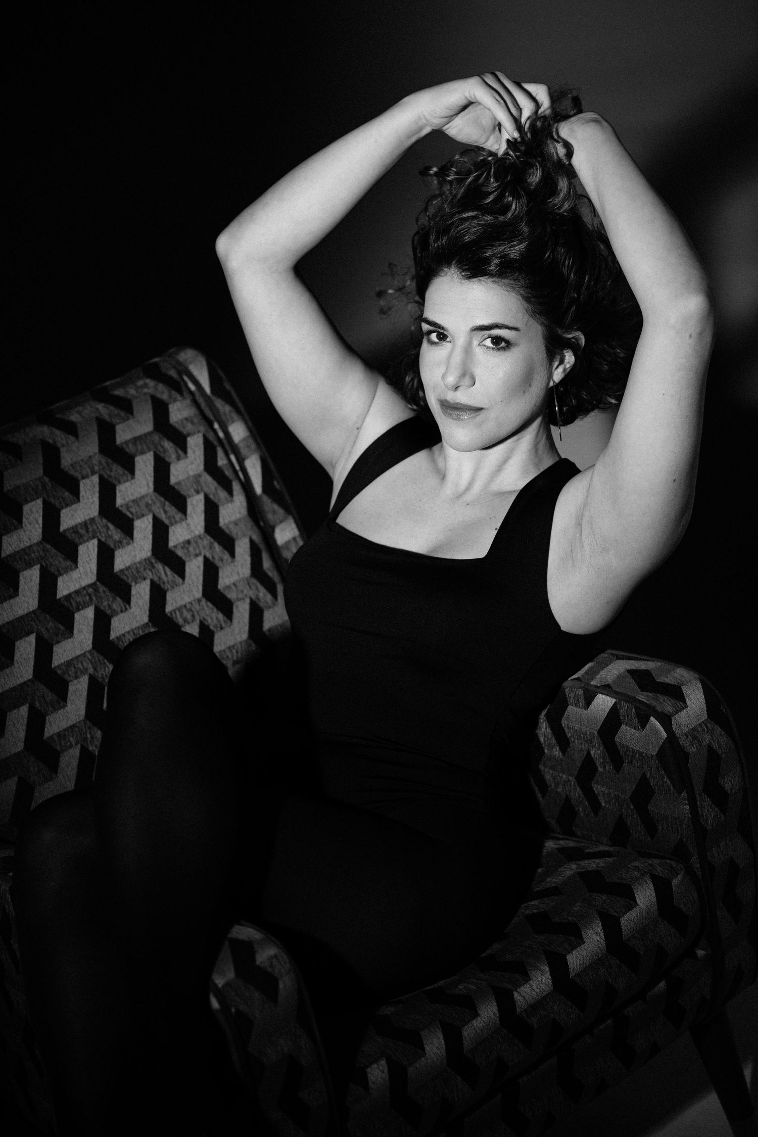 Dramatic black and white portrait with arms raised in artistic pose against dark background.