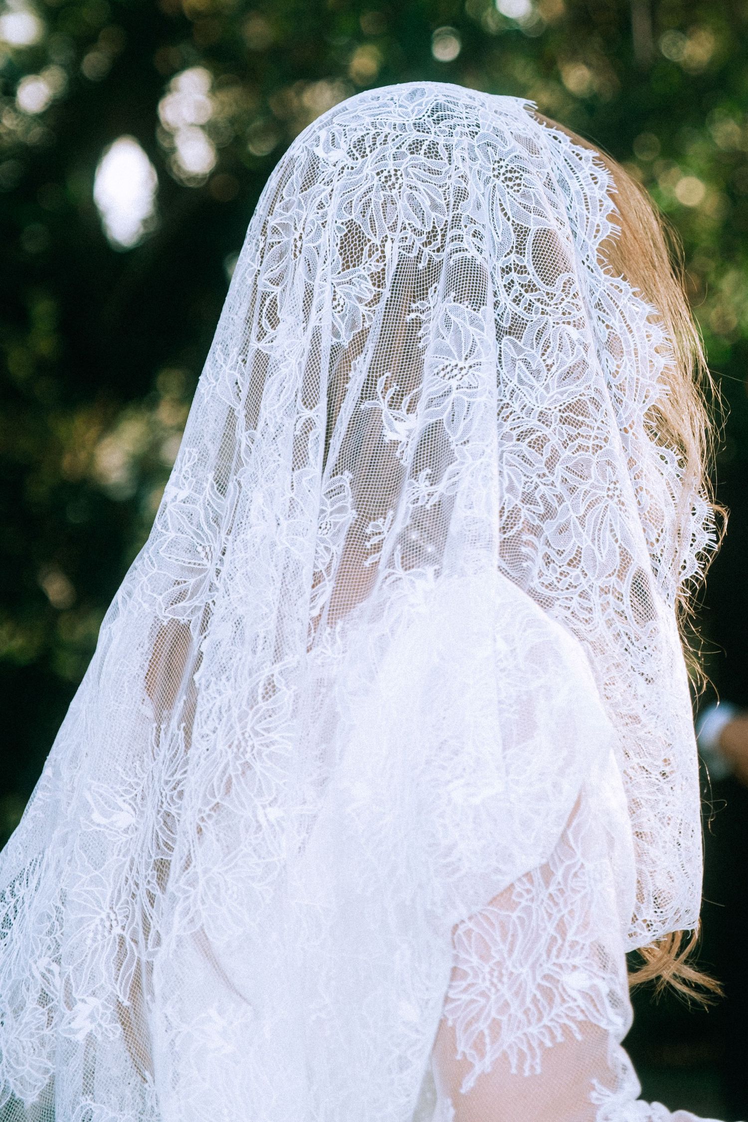 Close-up of delicate white lace bridal veil with floral pattern details against blurred natural background.
