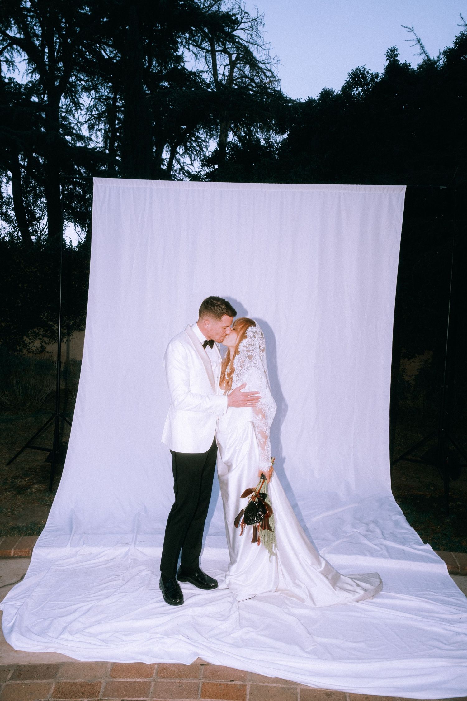 Artistic wedding portrait of couple against white backdrop in outdoor setting.