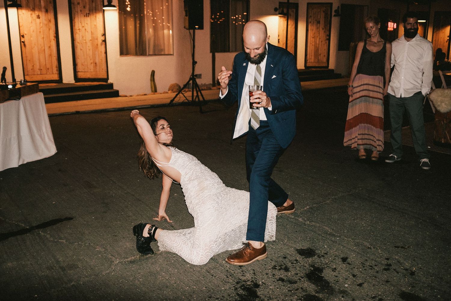 A couple performs a dramatic dance move during a wedding reception on a dark dance floor.