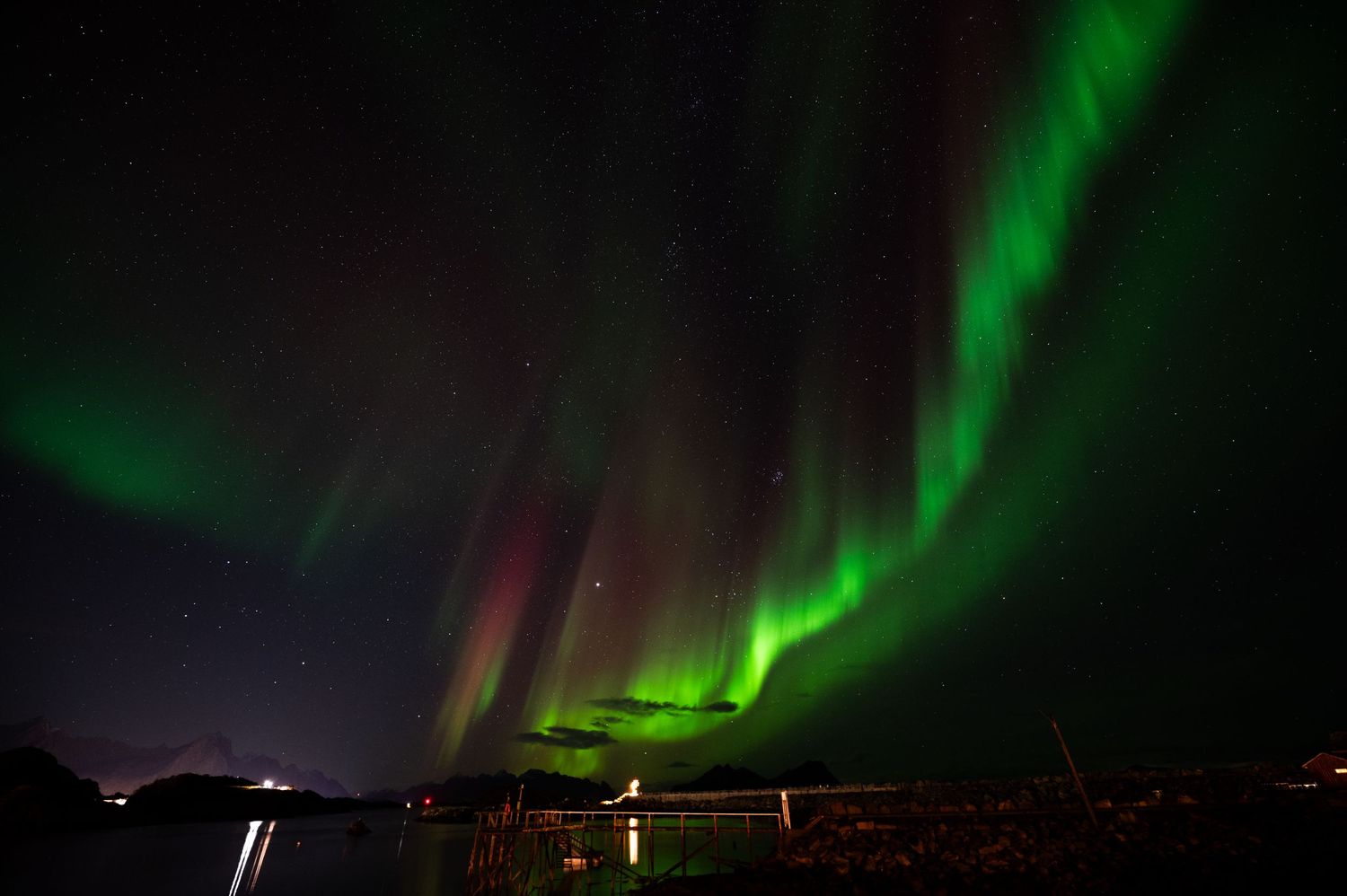 Northern lights display green ribbons of light over a coastal village at night.